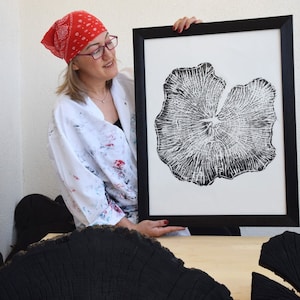 May include: A black and white print of a tree ring pattern in a black frame. The print is on white paper and is being held by a person wearing a white lab coat and a red bandana.