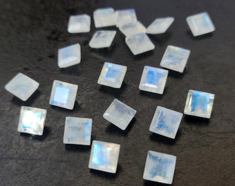 May include: A collection of 18 iridescent white moonstone square cabochons. The stones are approximately 10mm x 10mm in size and have a smooth, polished finish.