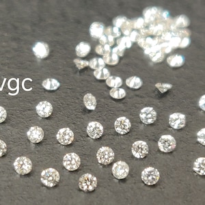 May include: A close-up image of a pile of loose round diamonds. The diamonds are scattered on a dark gray surface. The text "vgc" is visible in the lower left corner of the image.