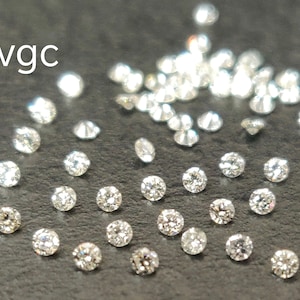 May include: A close-up image of a group of loose diamonds on a gray surface. The diamonds are round and have a brilliant cut. The text "vgc" is visible in the upper left corner of the image.