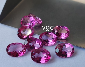 Könnte beinhalten: Eine Gruppe von neun ovalen rosafarbenen Edelsteinen, wahrscheinlich Rubine oder Spinelle, auf einer silbernen Oberfläche. Die Edelsteine sind facettiert und haben einen hohen Glanz. Der Text "vgc" ist auf dem Bild sichtbar.