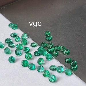 Puede incluir: Una colección de piedras preciosas verdes, probablemente esmeraldas, esparcidas sobre una superficie blanca. El texto "vgc" es visible en el fondo.
