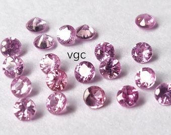 Puede incluir: Un conjunto de gemas rosas redondas y facetadas dispersas sobre una superficie blanca. Las gemas varían ligeramente en tonalidad. El texto "vgc" es visible.