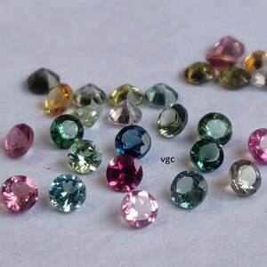 Puede incluir: Surtido de piedras preciosas redondas y facetadas en varios colores, incluyendo rosa, verde, azul y amarillo. Las piedras preciosas est&aacute;n dispuestas sobre una superficie blanca.