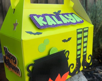 May include: A green and purple Halloween treat box with a cauldron, witch's legs, and bats. The box has a handle and says "Happy Halloween" and "KALAYA" on it.