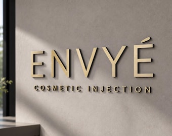 May include: A wall-mounted sign featuring the word ENVYÉ in large, gold-colored, three-dimensional capital letters, with the words COSMETIC INJECTION in smaller, matching gold-colored capital letters positioned directly underneath the main text.