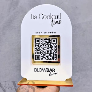 Könnte beinhalten: Ein weißes und goldenes Schild mit dem Text "Its Cocktail time" und "scan to order". Ein QR-Code befindet sich in der Mitte. Auf dem Schild steht auch "BLOWBAR lane". Das Schild wird von einer Hand gehalten.