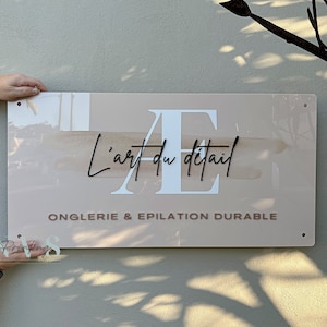 custom rectangle acrylic business sign wall, beige blush pink acrylic backing with logo on it, AE printed in white, business name in 3D black acrylic across, business tagline in 3D taupe acrylic along the bottom with 4 mounting holes on each corners