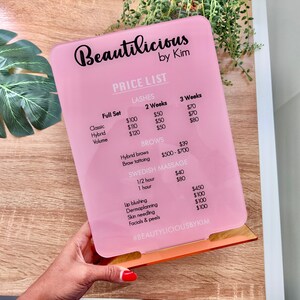 May include: Pink price list sign with the business name "Beautilicious by Kim" and a list of services and prices for lashes, brows, Swedish massage, lip blushing, dermaplanning, skin needling, and facials & peels.