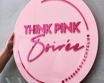 May include: Pink round sign with the text "Think Pink Soirée" and the text "@warregoyachtclub" in a smaller font.