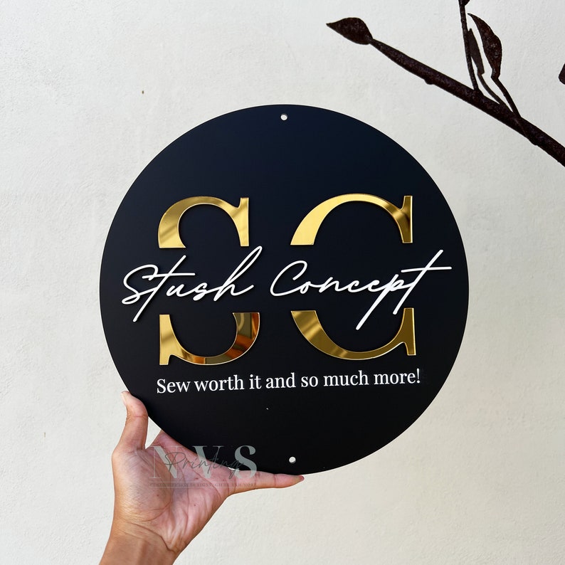 A round acrylic business sign in black acrylic backing, with SC in 3D gold mirror acrylic in serif font, Stush Concept in cursive font and in 3D gloss white acrylic, followed with business tagline on the bottom, mounting holes on top and bottom