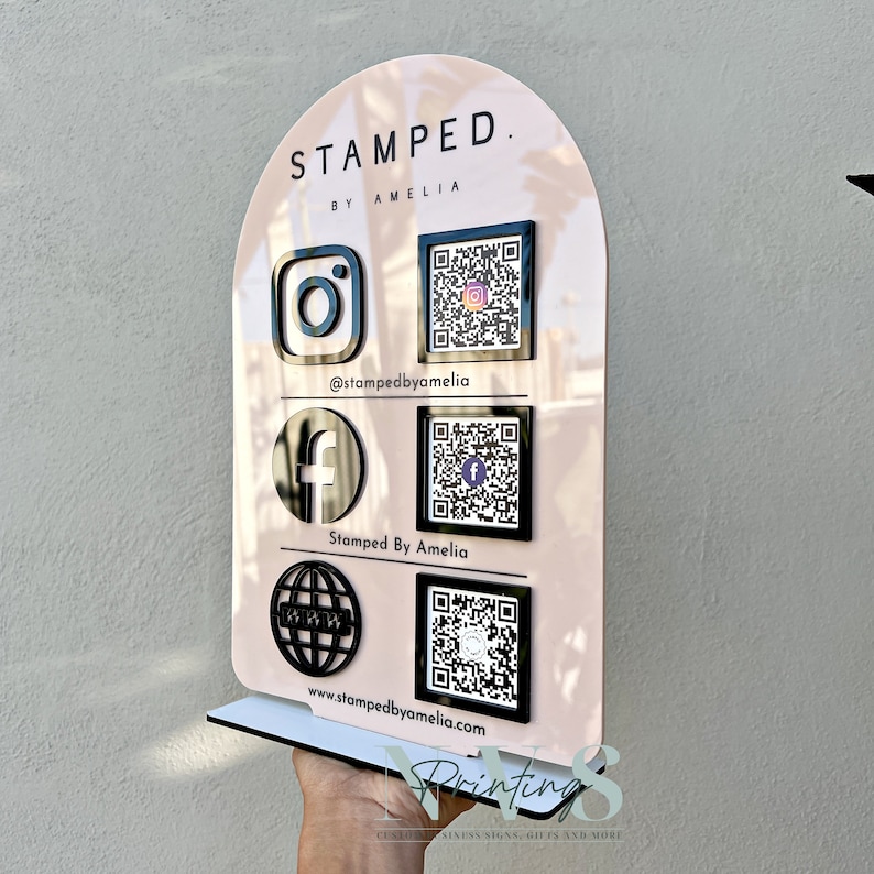 arch QR Code social media display stand in blush pink acrylic, business logo on top, 3D instagram facebook website logo in black acrylic along with each QR codes on the left, instagram facebook handle and website address written under QR code