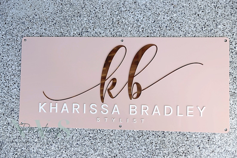 Custom Rectangle acrylic business sign in blush pink acrylic backing, initial KB in cursive font on top in 3D rose gold mirror, followed by KHARISSA BRADLEY under it in 3D gloss white acrylic in sans font, STYLIST on the bottom in sans font in white