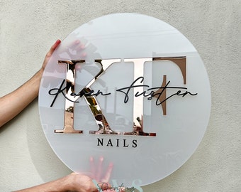 May include: A round, frosted white acrylic sign with the initials "KF" in rose gold, the name "Karen Fusten" in black script, and the word "NAILS" in black below.