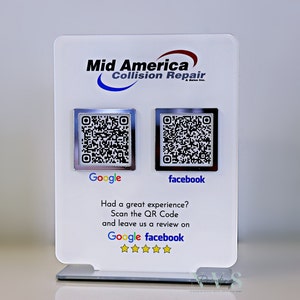 Op de afbeelding: Een wit bord met de tekst "Mid America Collision Repair" en twee QR-codes. De QR-code links is gelabeld "Google" en de QR-code rechts is gelabeld "facebook". Het bord bevat ook de tekst "Had a great experience? Scan the QR Code and leave us a review on Google facebook" en vijf sterren.