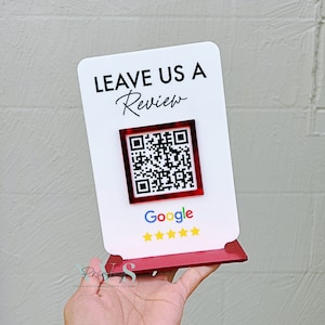 May include: White sign with the text "LEAVE US A Review" and a Google QR code. The sign has a red base and five gold stars.