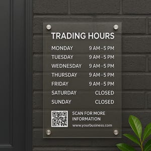 May include: A clear acrylic sign displaying business trading hours, mounted on a dark gray brick wall. The sign lists hours for each day of the week, with a QR code and website address for more information.
