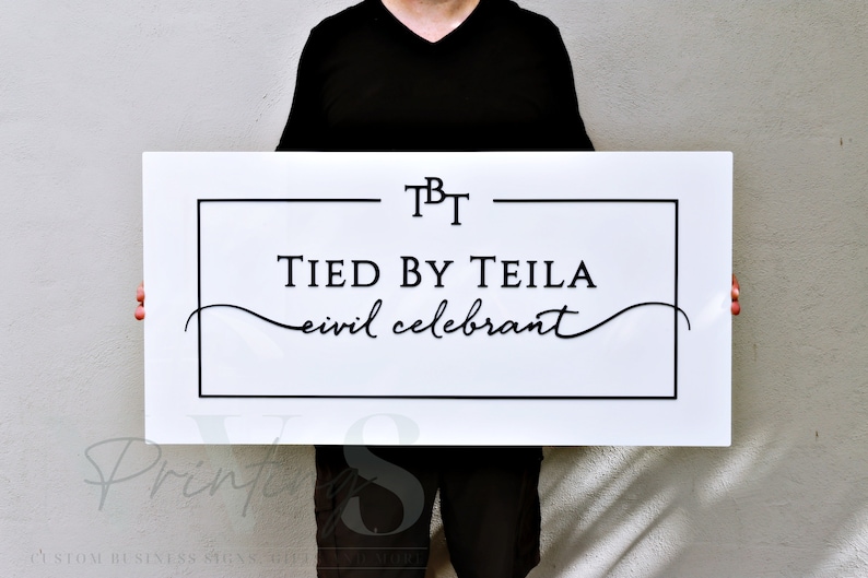 Custom Rectangle acrylic business sign in gloss white backing, with 3D black acrylic logo, TBT in serif font on top, black rectangle frame, TIED BY TEILA inside the frame in serif font, CIVIL CELEBRANT in cursive font