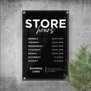 May include: Black rectangular store hours sign with white text. The sign displays the store's hours of operation for each day of the week, from Monday to Friday, 10 AM to 4 PM. Saturday and Sunday are closed. The sign also includes a business logo and contact information.