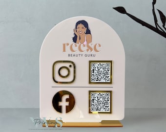 May include: White arch-shaped sign with the text "Reese Beauty Guru" and a cartoon illustration of a woman. The sign also includes social media icons for Instagram and Facebook, along with QR codes.