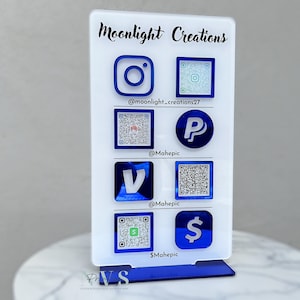 May include: A white acrylic sign with the text "Moonlight Creations" at the top. The sign has blue icons for Instagram, PayPal, Venmo, and Cash App, along with QR codes for each platform. The sign is on a blue base.