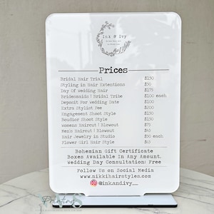 May include: White sign with black text listing prices for hair styling services. The sign reads "Ink & Ivy" and lists prices for services such as bridal hair trial, styling in hair extensions, day of wedding hair, bridesmaids, bridal tribe, deposit for wedding date, extra stylist fee, engagement shoot style, boudoir shoot style, women's haircut and blowout, men's haircut and blowout, hair jewelry in studio, and flower girl hair style. The sign also includes the text "Bohemian Gift Certificate Boxes Available In Any Amount. Wedding Day Consultation: Free" and "Follow Us on Social Media www.nikkihairstyles.com @ink.and.ivy_"