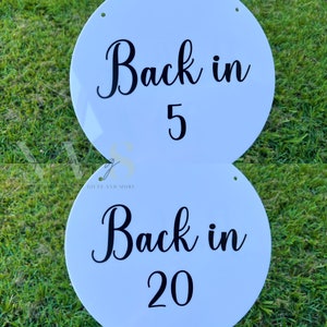 Peut inclure: Deux panneaux ronds blancs avec du texte noir. Le panneau du haut indique "Back in 5" et le panneau du bas indique "Back in 20".
