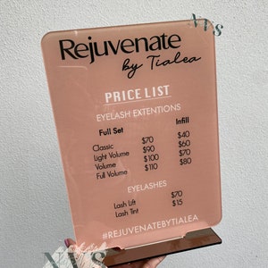 May include: A pink acrylic sign with the text "Rejuvenate by Tialea" and a price list for eyelash extensions and lash services. The prices are listed in US dollars. The sign has a hashtag at the bottom that reads "#REJUVENATEBYTIALEA".