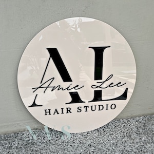 A round business sign with beige acrylic backing, 3D gloss black acrylic for the logo that says AL in capital letters, Amy Lee in the middle in cursive font and HAIR STUDIO on the bottom in serif font