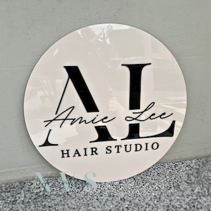 A round business sign with beige acrylic backing, 3D gloss black acrylic for the logo that says AL in capital letters, Amy Lee in the middle in cursive font and HAIR STUDIO on the bottom in serif font