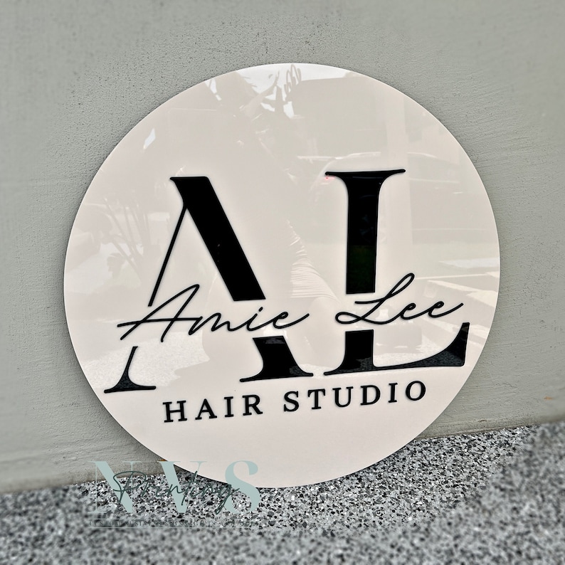 A round business sign with beige acrylic backing, 3D gloss black acrylic for the logo that says AL in capital letters, Amy Lee in the middle in cursive font and HAIR STUDIO on the bottom in serif font