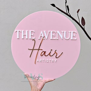 Round business sign in pink background with 3D white acrylic and rose gold acrylic, THE AVENUE in 3D gloss white acrylic serif font, Hair in 3D rose gold mirror cursive ant and ARTISTRY in 3D gloss white in sans font