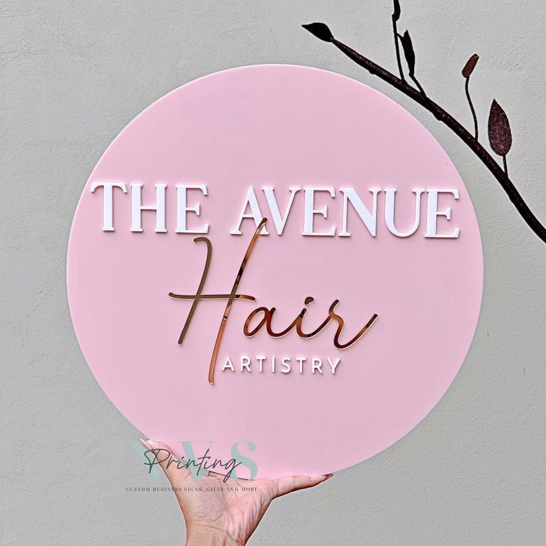 Round business sign in pink background with 3D white acrylic and rose gold acrylic, THE AVENUE in 3D gloss white acrylic serif font, Hair in 3D rose gold mirror cursive ant and ARTISTRY in 3D gloss white in sans font