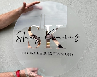 Könnte beinhalten: Ein rundes, mattes Glasschild mit dem Text "Stacey Kearns" in schwarzer Kursivschrift und "SK" in roségoldenen Buchstaben. Der Text "Luxury Hair Extensions" ist in Schwarz unter den Initialen gedruckt.