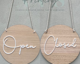 May include: Two round wooden signs with rope hangers. The sign on the left says "Open" in white script. The sign on the right says "Closed" in white script.