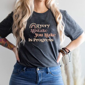 May include: A dark gray t-shirt with a rainbow graphic and the text "Every Mistake You Make Is Progress".