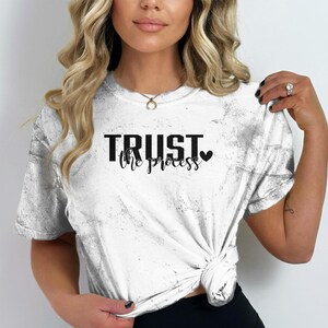 May include: White t-shirt with a distressed look and the text "TRUST the process" in black with a small black heart.
