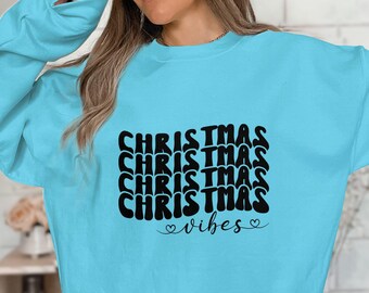 May include: A light blue sweatshirt with the text "CHRISTMAS vibes" in black lettering. The word "CHRISTMAS" is repeated four times in a stacked, wavy font.
