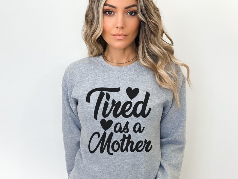 Op de afbeelding: Grijs sweatshirt met de tekst "Tired as a Mother" in zwarte cursieve letters met drie zwarte harten.