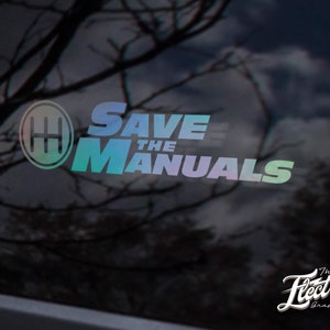 Peut inclure: Un autocollant avec un dégradé arc-en-ciel qui dit "SAVE THE MANUALS" avec une icône de motif de changement de vitesse. L'autocollant est sur une vitre de voiture noire. Le texte "The Electric Graphic Co." est en blanc sous l'autocollant.