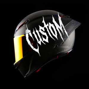 Puede incluir: Casco de moto negro con visera dorada y la palabra "CUSTOM" en letras blancas estilizadas. El casco tiene un diseño geométrico en la parte trasera y está fabricado en Italia.