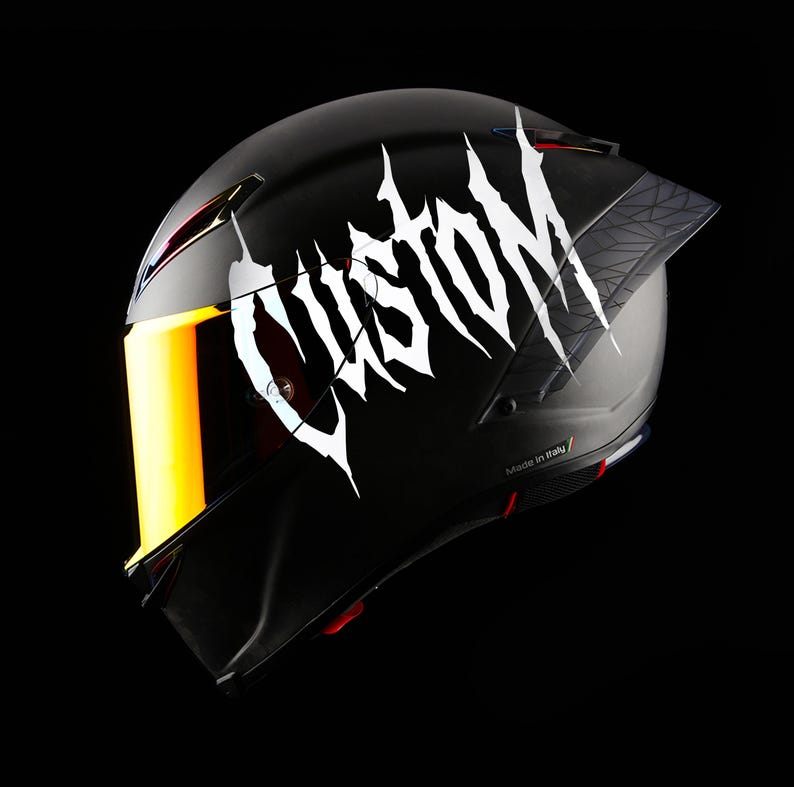 May include: Black motorcycle helmet with a gold visor and the word "CUSTOM" in white, stylized lettering. The helmet has a geometric design on the rear and is made in Italy.