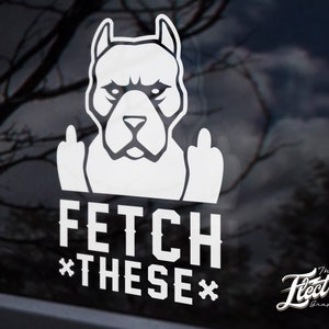Op de afbeelding: Witte vinyl sticker met een cartoon pitbull hond die de middelvinger opsteekt met de tekst "FETCH THESE" eronder. De sticker zit op een zwart autoruit.