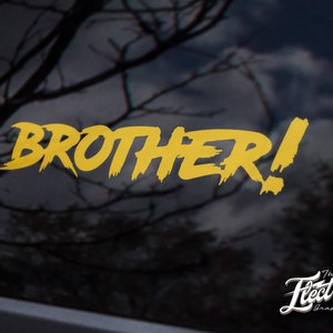 May include: A gold vinyl decal with the word "BROTHER!" in a bold, stylized font. The decal is on a black background with a blurred image of tree branches in the background.
