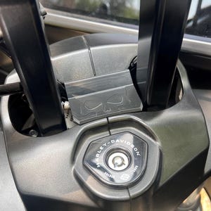 May include: Close-up of a motorcycle's handlebar area, featuring a Harley-Davidson ignition switch. The black components include the handlebars, a skull-shaped accent, and the ignition switch with the Harley-Davidson logo.