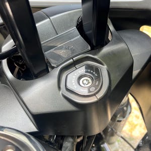 May include: Close-up of a black motorcycle ignition switch with the Harley-Davidson logo. The keyhole is visible, and the switch is surrounded by black plastic components. The image is taken from a slightly elevated angle.