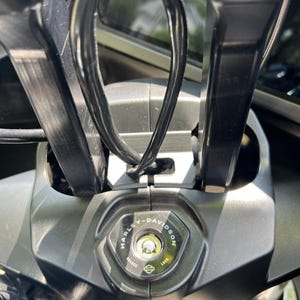 May include: Close-up of a motorcycle's ignition switch, featuring the Harley-Davidson logo. The switch is surrounded by black handlebars and wiring. The keyhole is illuminated, and the switch has "UNLOCK" and "LOCK" indicators.
