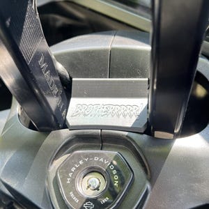May include: Close-up of a motorcycle's ignition area. The Harley-Davidson ignition switch is visible, along with a metal plate that reads "BROTHERRRR!" and a black handlebar. The words "MADE IN" are also visible.