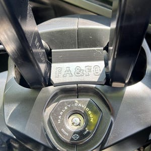 May include: Close-up of a black Harley-Davidson motorcycle ignition switch and handlebars. The ignition switch is hexagonal with the Harley-Davidson logo and the words "Unlock" and "Lock". The handlebars have the text "FA & FO" and "MADE IN ITALY".