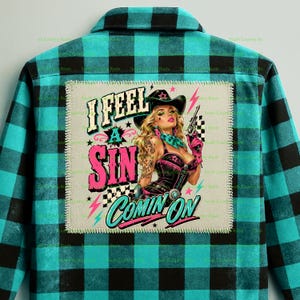 May include: A teal and black buffalo plaid button-down shirt featuring a large square patch on the back. The patch displays a cowgirl holding a revolver with the text I FEEL A SIN COMIN ON in bold pink, white, and teal lettering with lightning bolts.